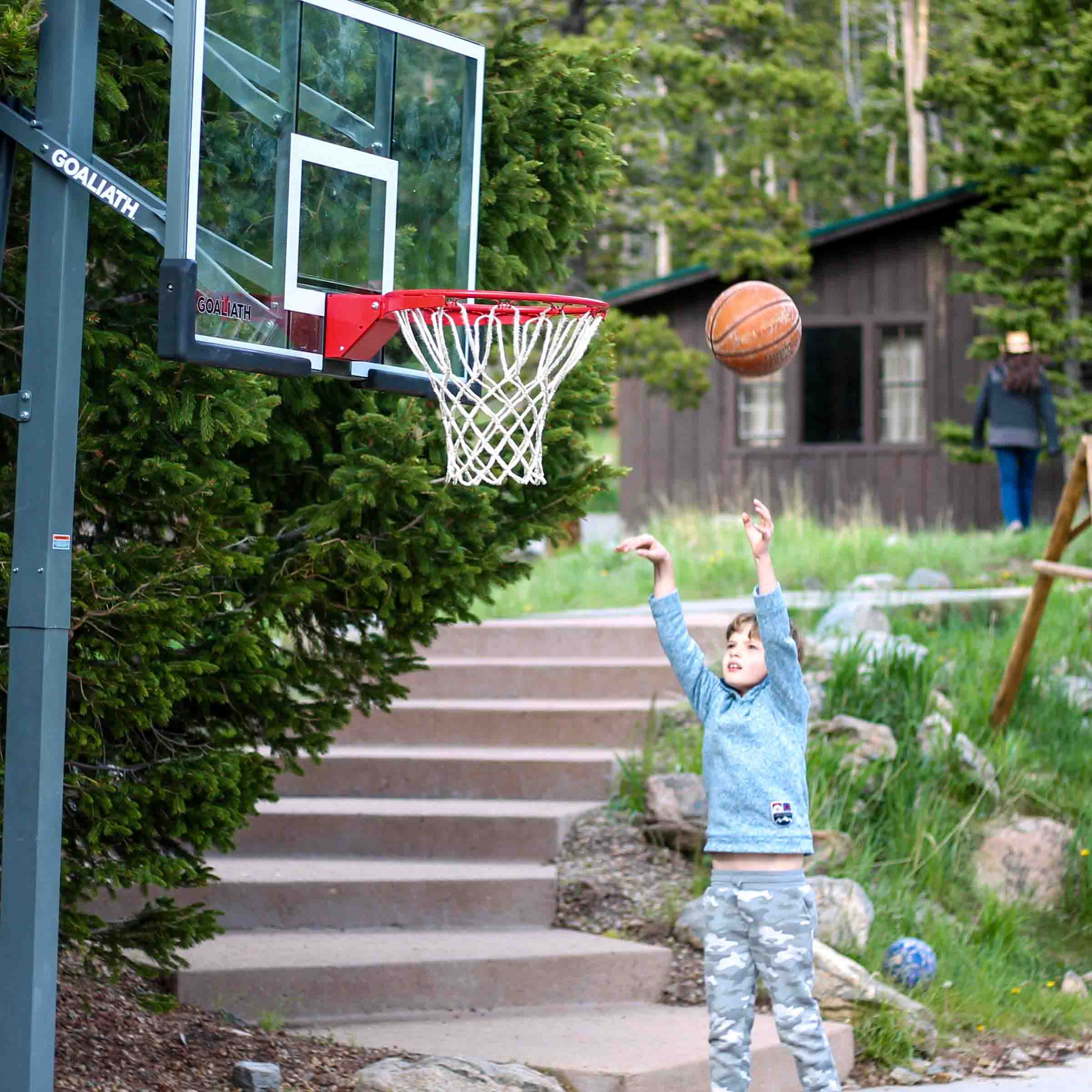 A young boy playing basketball on an outdoor court in front of a building.