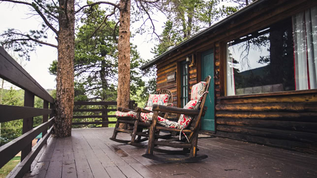 Two wooden rocking chairs with floral cushions on a wooden deck outside a log cabin.