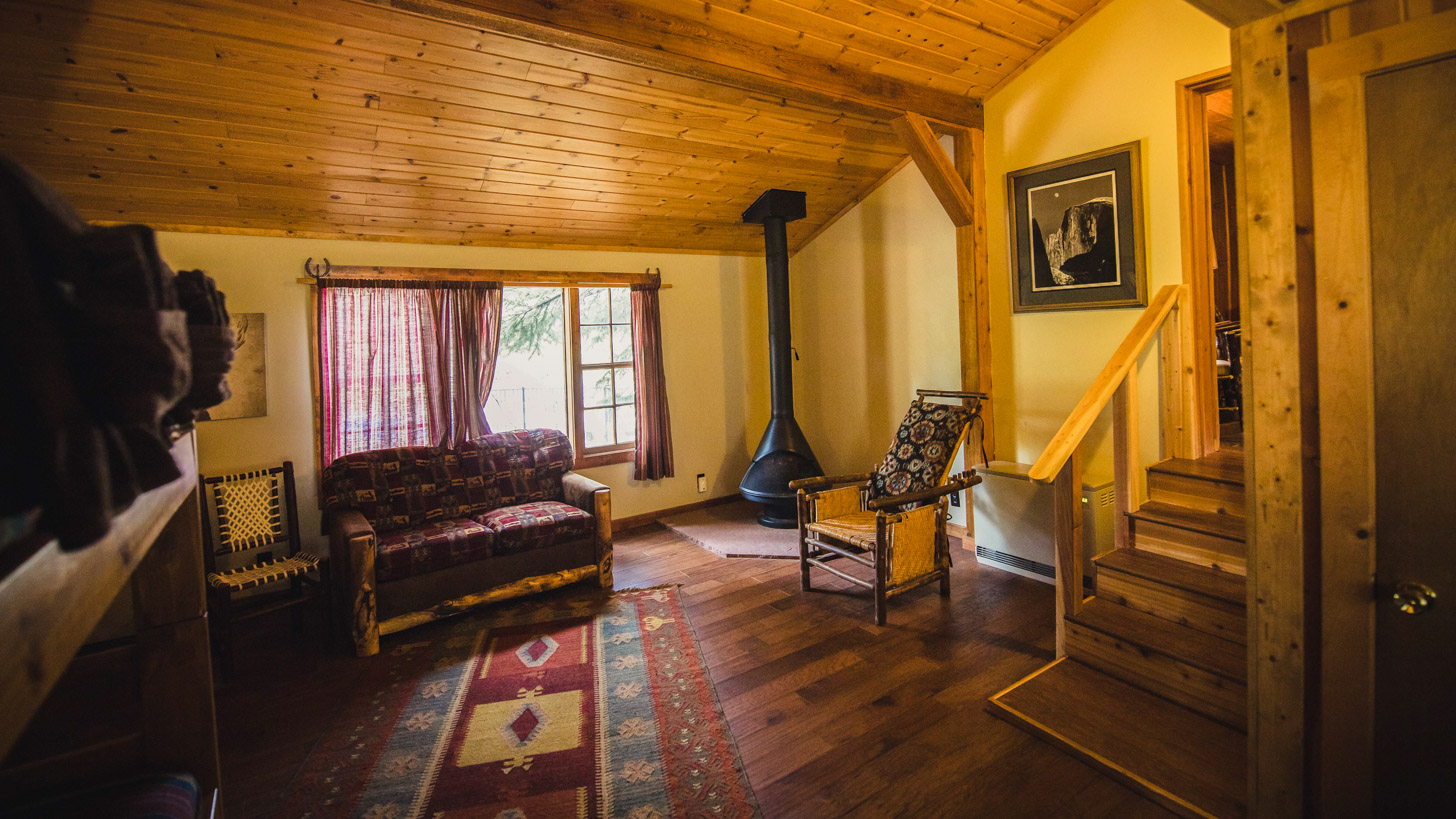 A cozy lobby with a wooden ceiling and floor, a sofa, chair, and staircase.