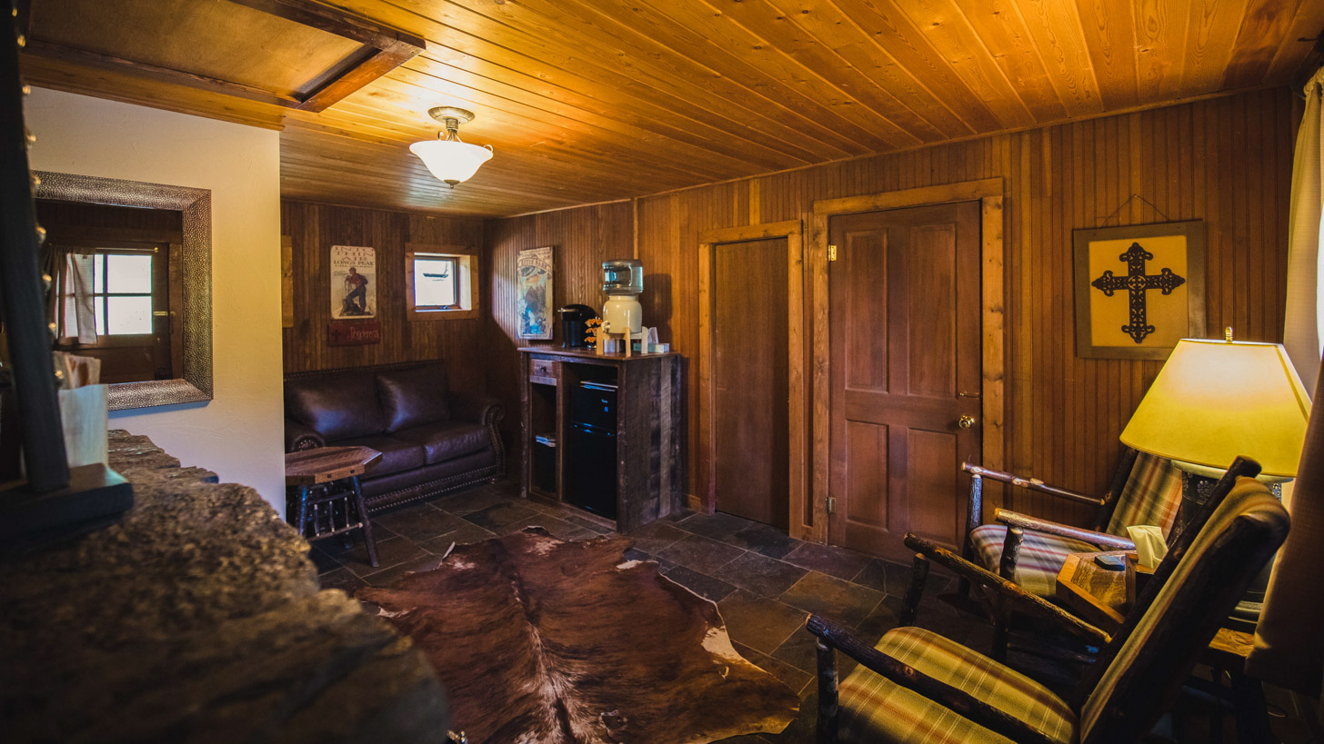 A cozy lobby with wood paneling, a leather sofa, and two plaid chairs.
