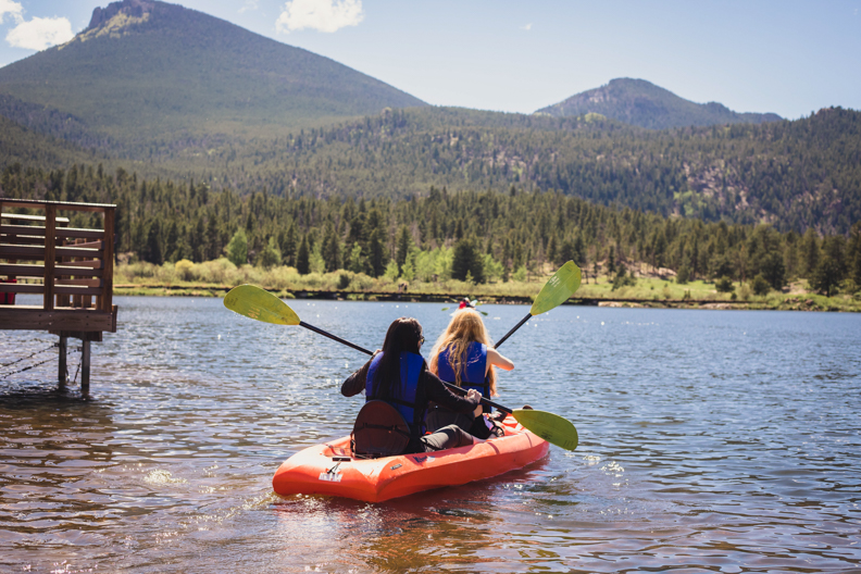 Two people in a kayak on a lake with mountains in the background.